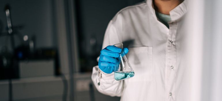 a person wearing gloves holding an Erlenmeyer flask with liquid