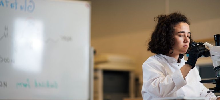 female scientist in a lab coat examines a sample under a microscope looking for semaglutide and tirzepatide differances