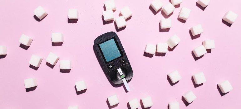 blood glucose meter surrounded by sugar cubes on a pink background, highlighting diabetes awareness