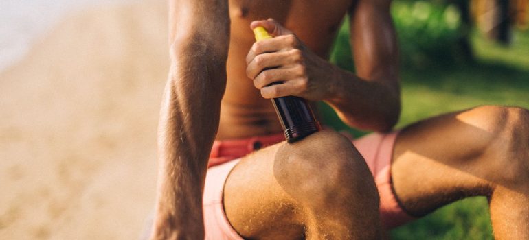 a close-up of a man applying tanning spray on a sunny beach day