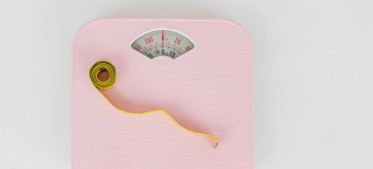 a pink weighing scale paired with a yellow measuring tape on a white backdrop