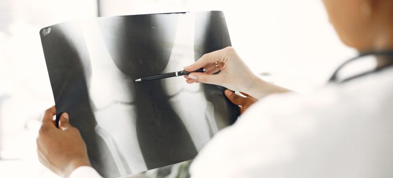 A medical professional closely examines a leg X-ray, pointing out details with a pen