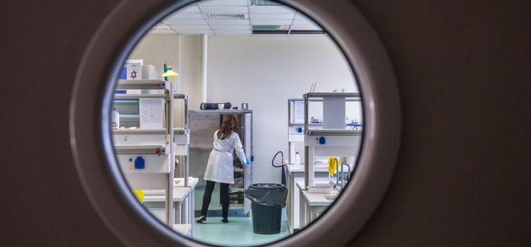a female scientist in a lab coat working inside a state-of-the-art laboratory through a circular window view